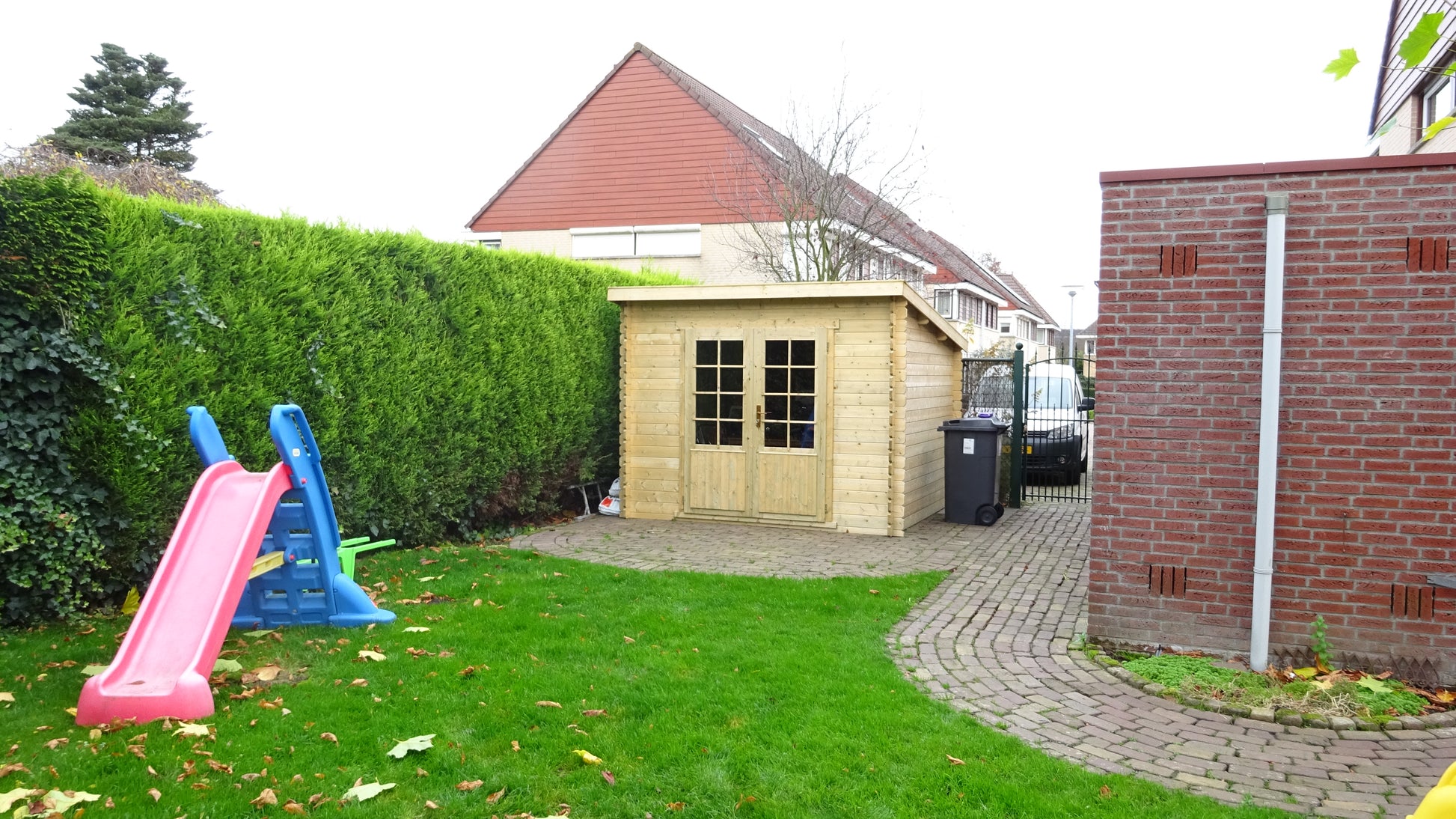 Houten Interflex 3020L tuinhuis in tuin met groen gras en kleurrijke glijbaan