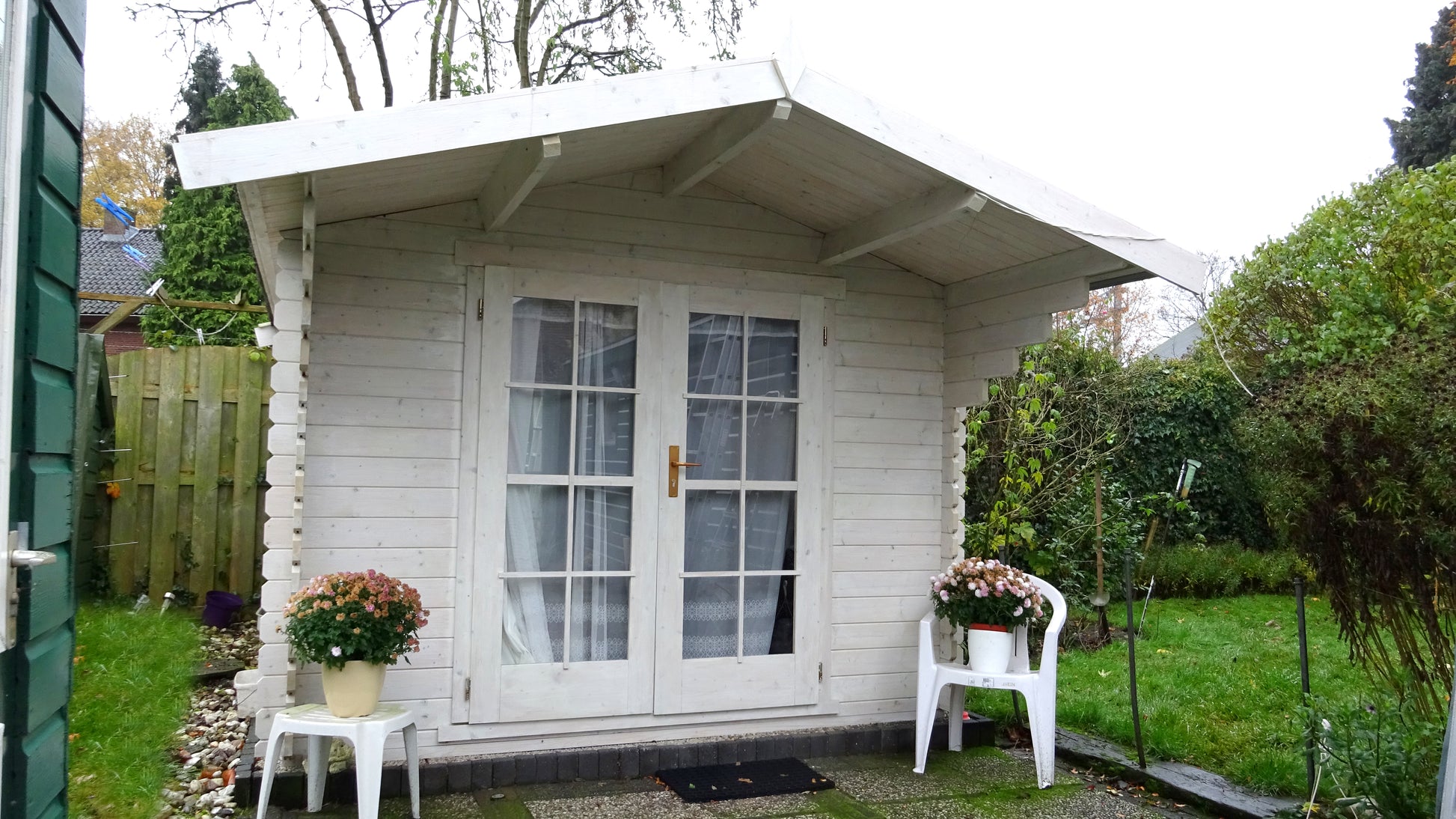 Wit geschilderd tuinhuis Interflex 3032 met veranda en stoel op grasveld
